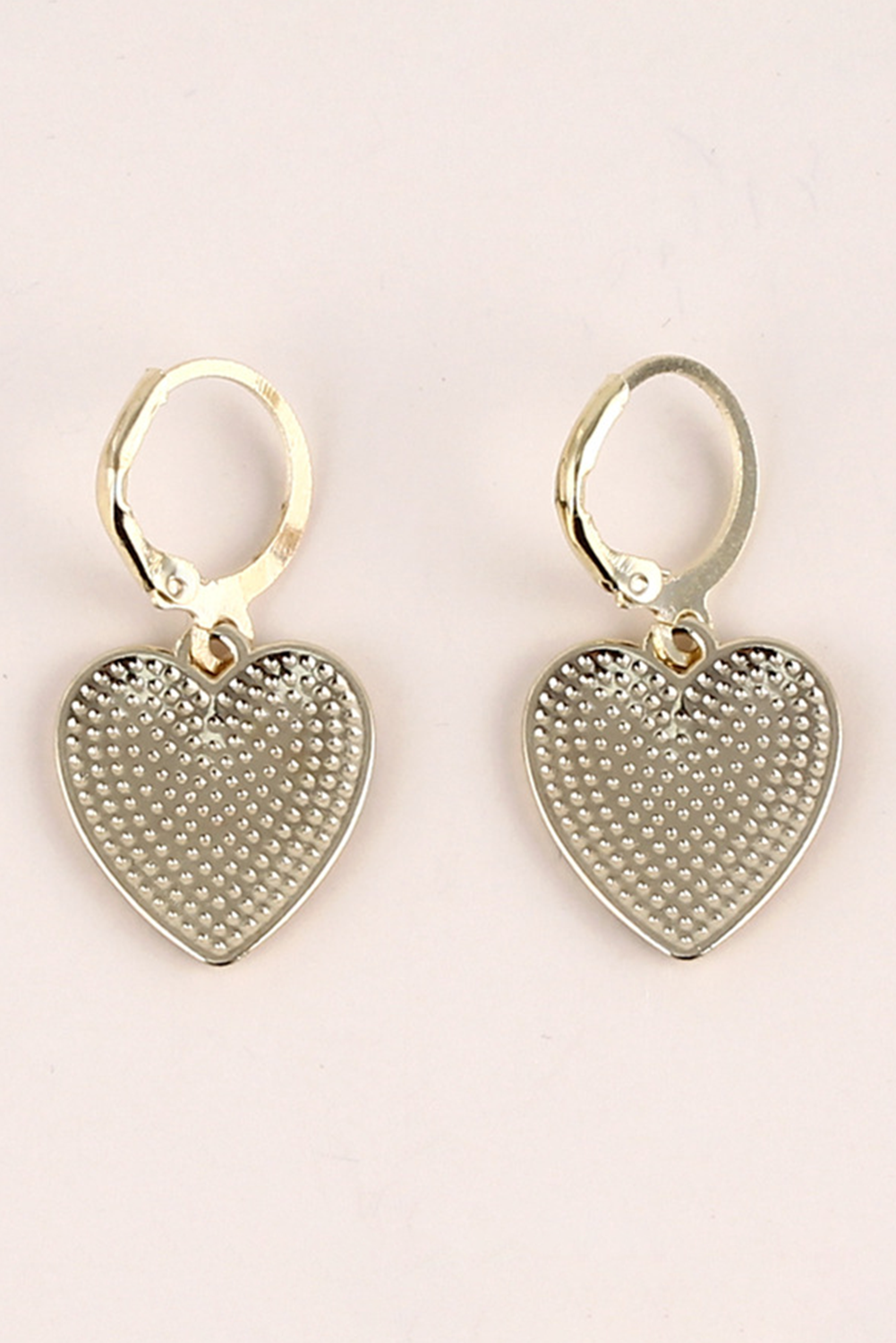 Heart-shaped silver earrings on a light pink background