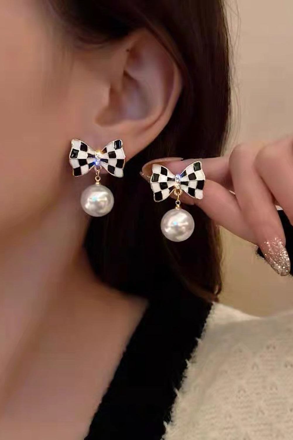 Close-up of a person wearing bow-shaped earrings with pearl drops.